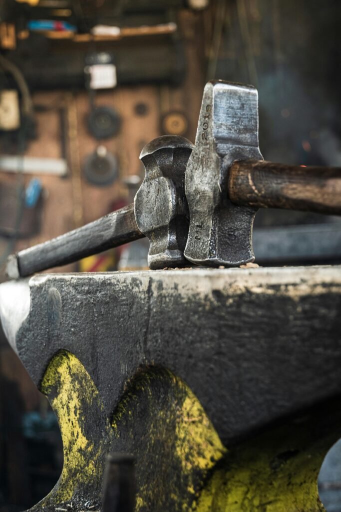 Detailed view of a hammer resting on an anvil in a blacksmith's workshop.